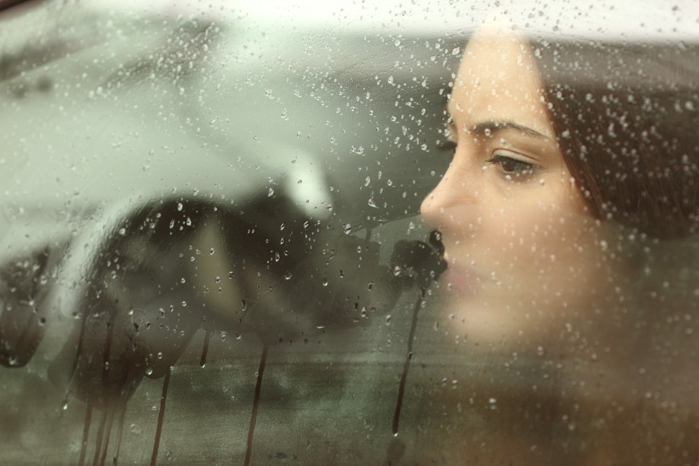 woman looks out window at rain
