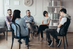 men and women seated in a circle as part of a group therapy session enjoying the 5 benefits of substance abuse treatment