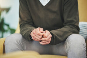 Close up of a man seated with hands clenched anxiously in front of him while awaiting process addiction treatment