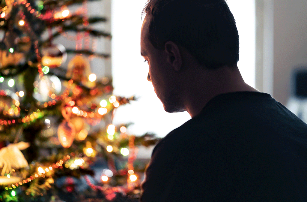 silhouette of a man standing in front of brightly lit Christmas tree struggling with depression and the holidays