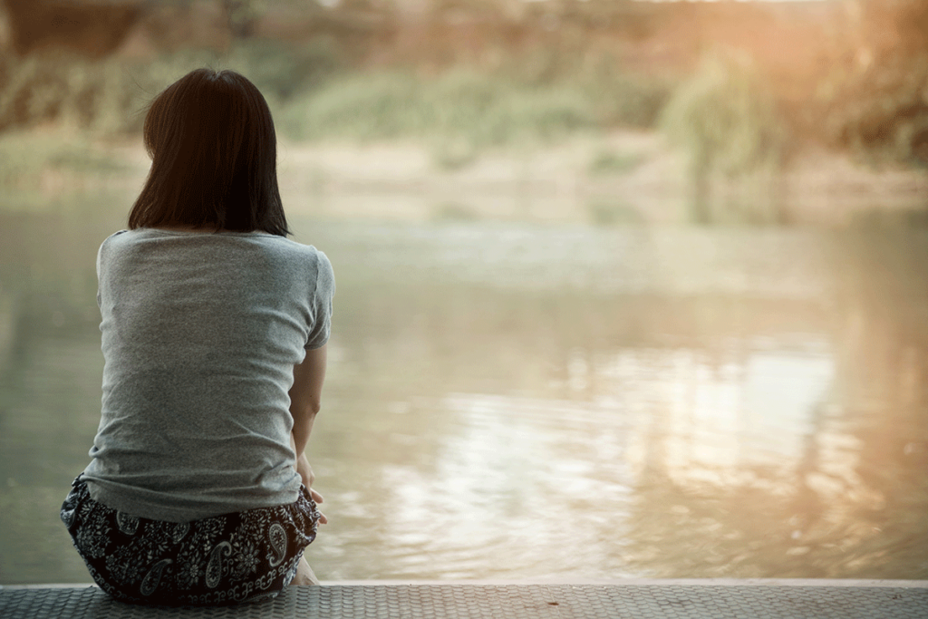 woman seated alone on a lake front facing the water with her back to the camera pondering how to deal with loneliness on Valentine's Day