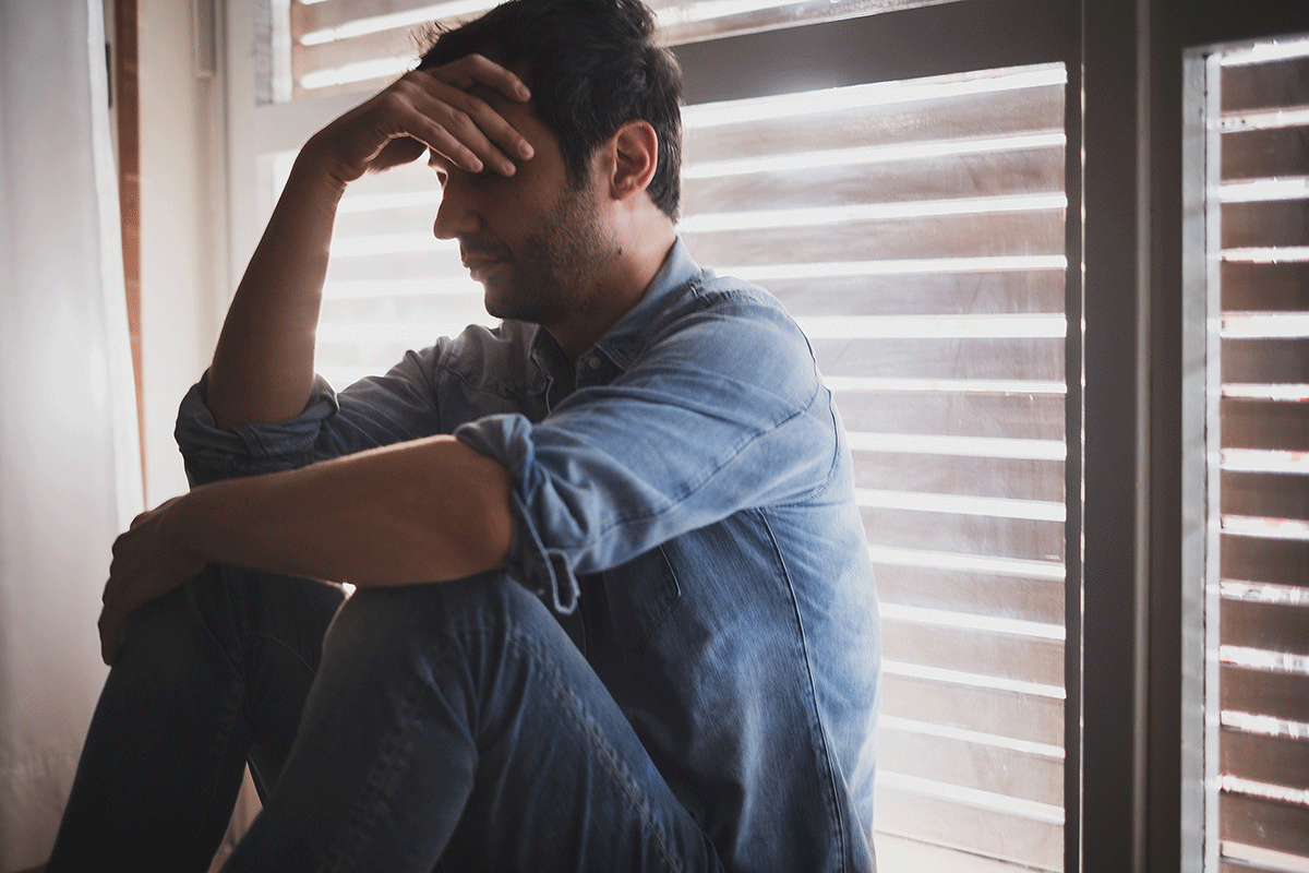 troubled young man seated in front of window with closed blinds with his head in his hands wondering how cocaine impacts anxiety