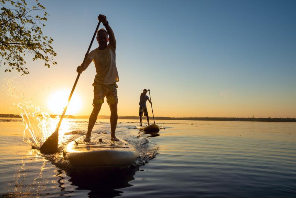 two people paddle boarding at sunset in calm waters as one of 7 outdoor activities to combat depression