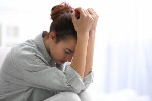 young distraught woman seated on floor leaning against wall in brightly lit room with her head in her hands experiencing fentanyl withdrawal symptoms.