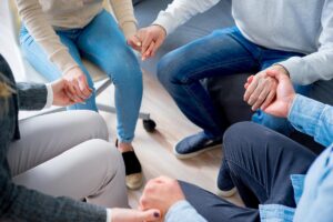 family members seated in a circle clasping hands as a demonstration of the importance of family support during treatment