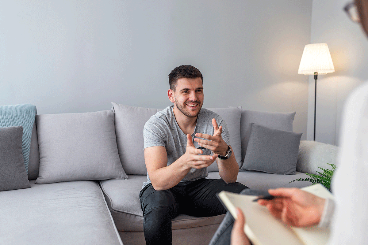 Smiling young man seated on couch in therapists's office eagerly discusses finding PTSD treatment in Georgetown, TX.