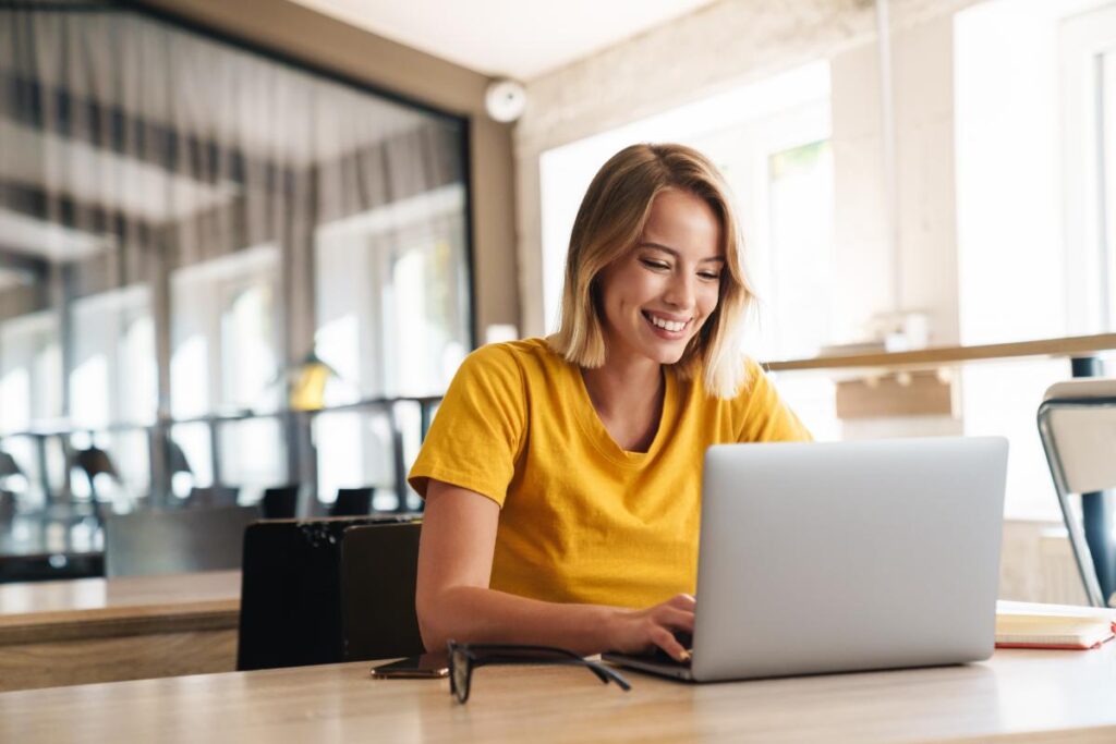 young smiling woman working on laptop at home while researching the 5 reasons life skills training is important