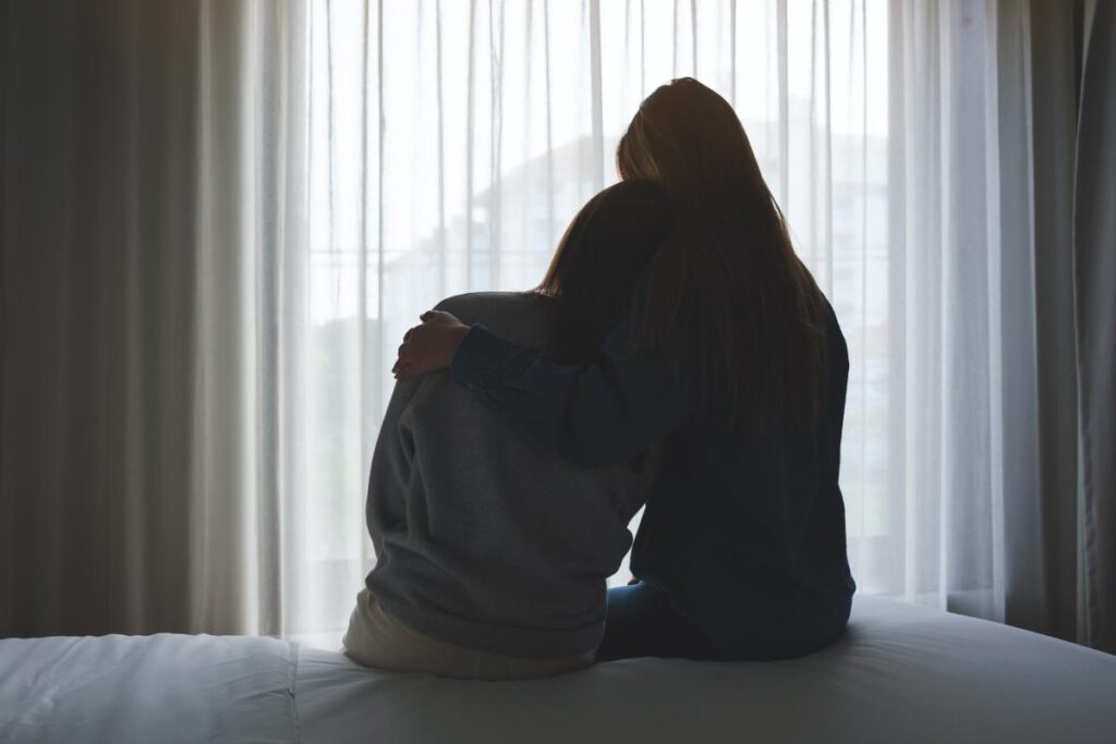 silhouette of two family members seated on a bed with one hugging the other and helping a loved one with a fentanyl addiction