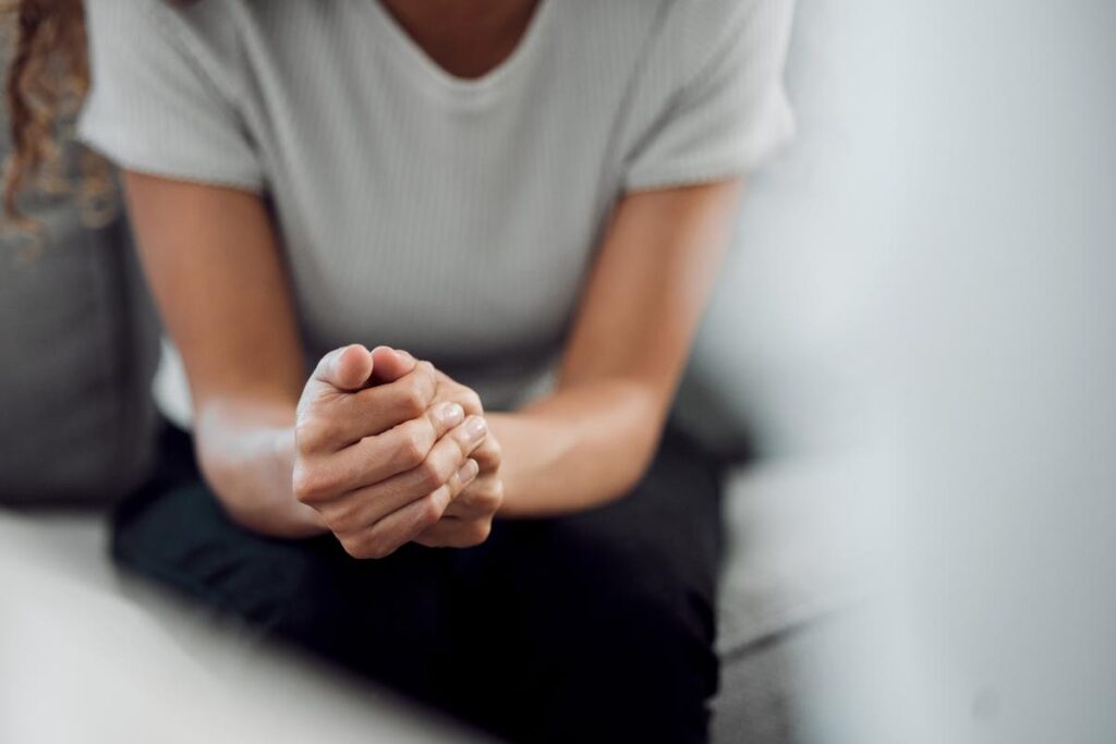 woman sitting pensively with her hands folded as she contemplates the signs of prescription drug abuse