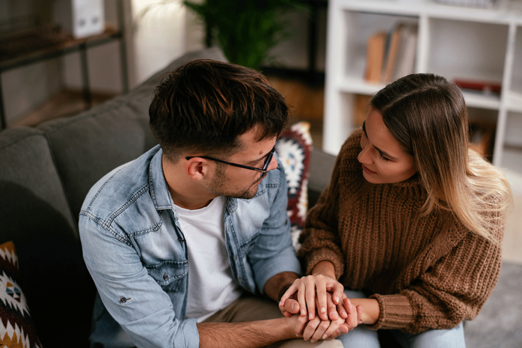 couple seated on couch clutching each other's hands in an behavioral health office learning that helping a loved one with alcohol addiction requires professional assistance.