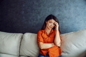 distraught young woman seated on couch in an office peparing to discuss how trauma influences substance use disorder