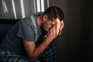 young man seated in darkened room with his head in his hands experiencing the dangers of benzodiazepine withdrawal