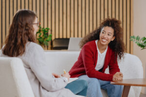 A woman participating in a women's rehab program is sitting across from her therapist and smiling.