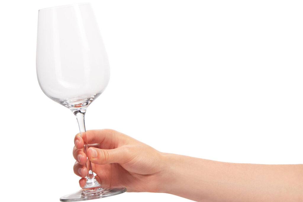A hand holds an empty wine glass. Someone is preparing to consume alcohol to handle symptoms of depression.