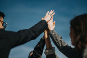 A group of people are high-fiveing one another outside. They are all participating in advocacy services and recovering well.