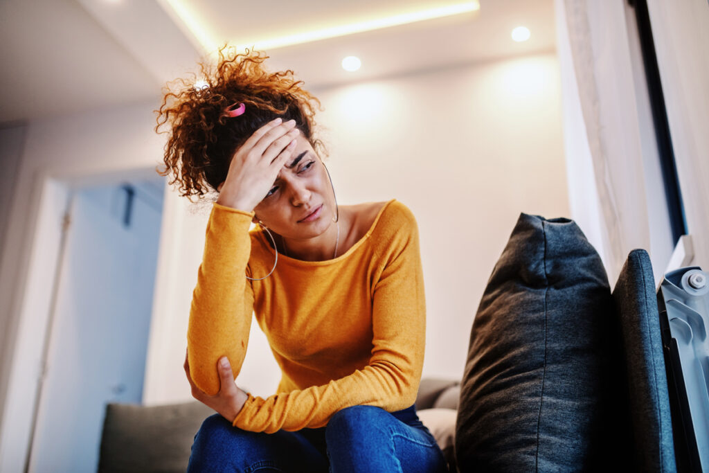 Woman holding head while sitting on couch